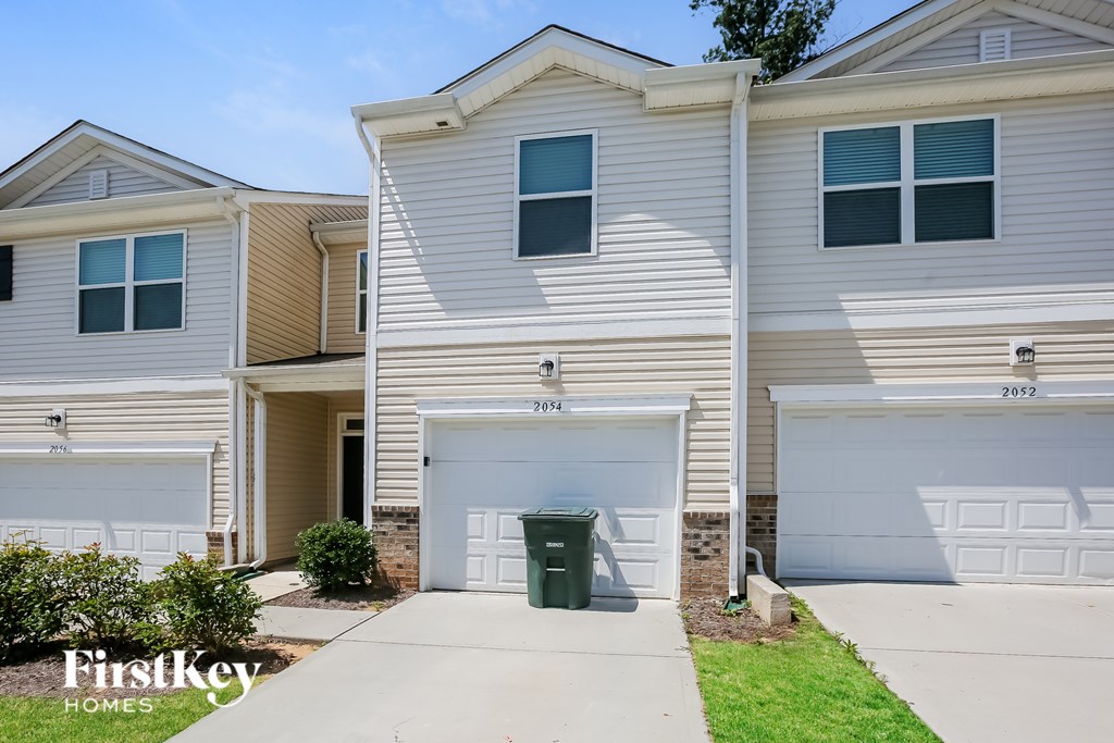 A two-story house with a garage and a green trash bin in front.