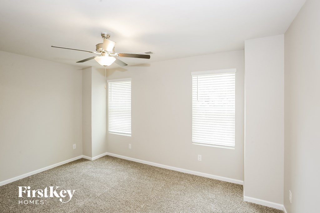 A room with a ceiling fan and two windows.