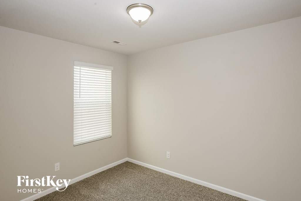 A room with a carpet floor, a window with blinds, and a light fixture on the ceiling.
