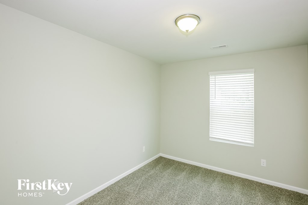 A room with a carpet floor, a window with blinds, and a light on the ceiling.