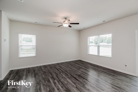 A spacious room with a ceiling fan and two windows.