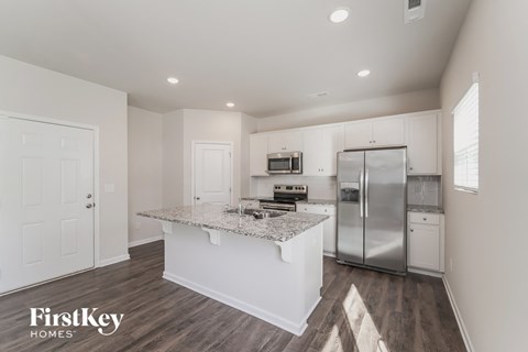 a white kitchen with a marble counter top and stainless steel refrigerator