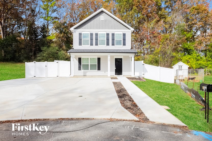 A house with a grey roof and a white fence in front of it.