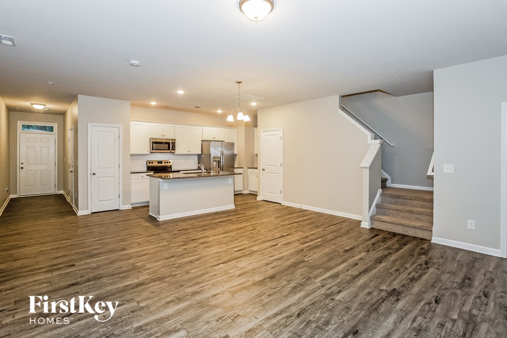 A spacious kitchen and living room with wooden flooring and white walls.