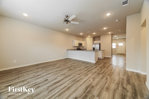 A spacious room with wooden flooring and a kitchen area in the background.