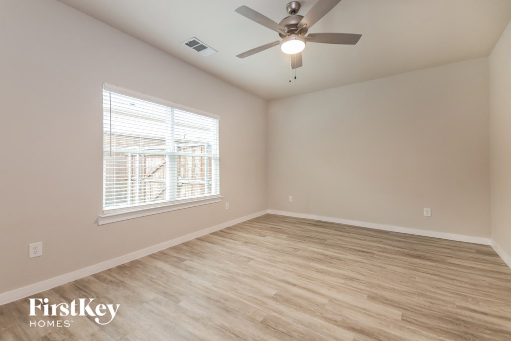the spacious living room with hardwood flooring and a ceiling fan