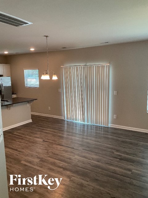 A room with wooden floors and a kitchen area with a refrigerator.