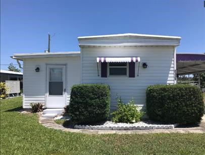 a small white house with a lawn and bushes