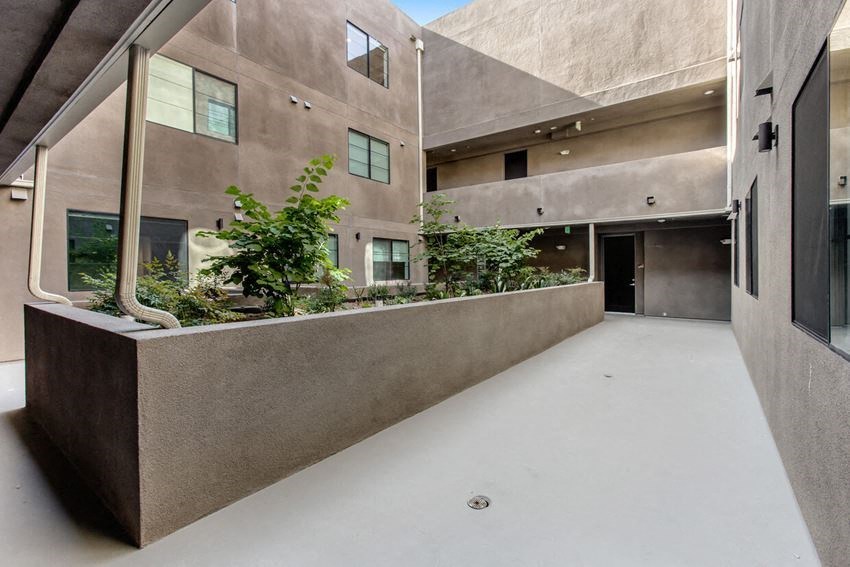 the courtyard of an apartment building with a concrete wall and plants in it
