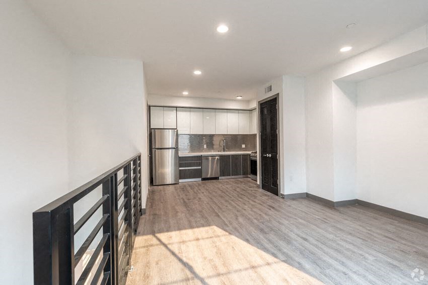 an empty living room with a kitchen in the background