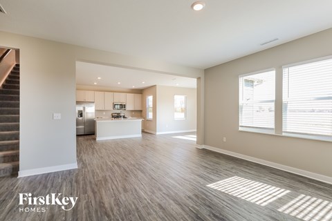 A spacious living room with a staircase on the left and a kitchen area in the background.
