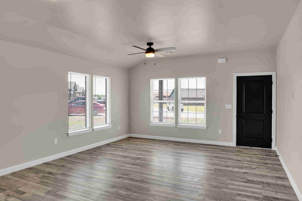 an empty living room with a ceiling fan and three windows