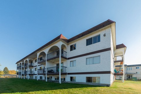 a large white apartment building with balconies and a green lawn