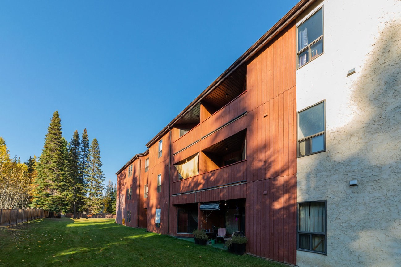 the side of a building with a wooden facade and a grass yard
