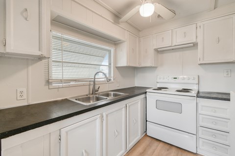A white kitchen with a black counter top and a white stove.