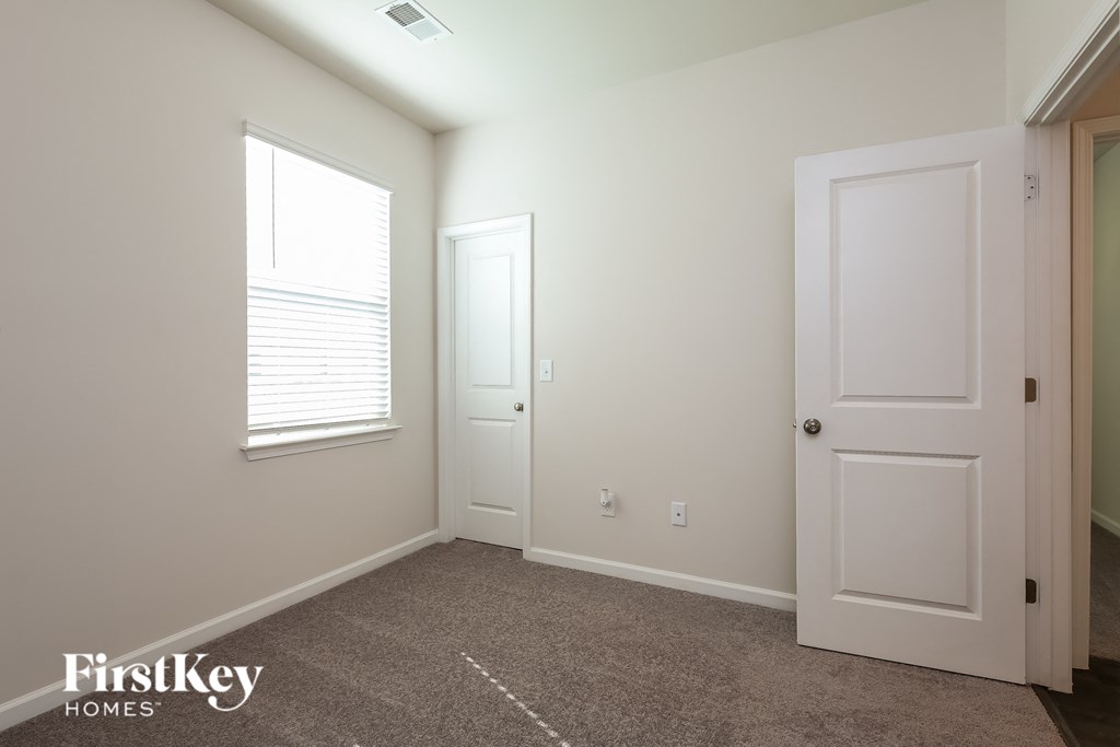 A room with a carpeted floor, two doors, and a window with blinds.