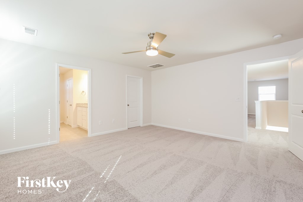 A spacious, empty room with a carpeted floor and a ceiling fan.