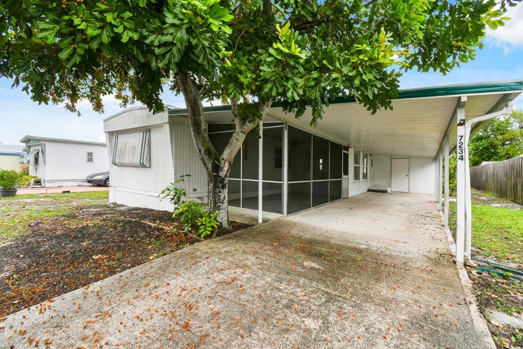 A white house with a green roof and a tree in front.