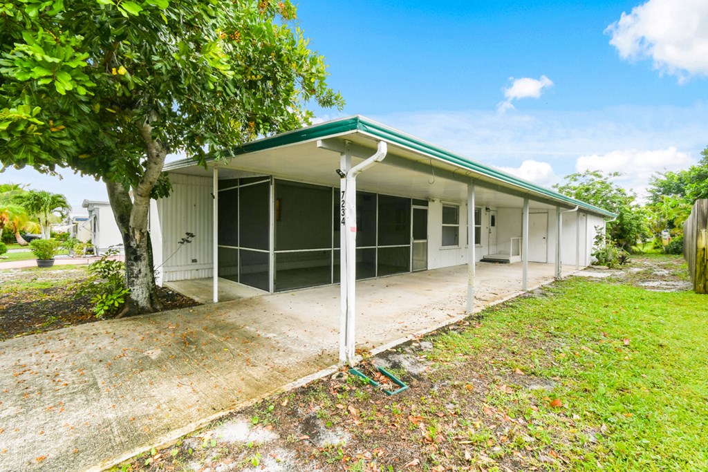 A white house with a green roof is surrounded by trees and grass.