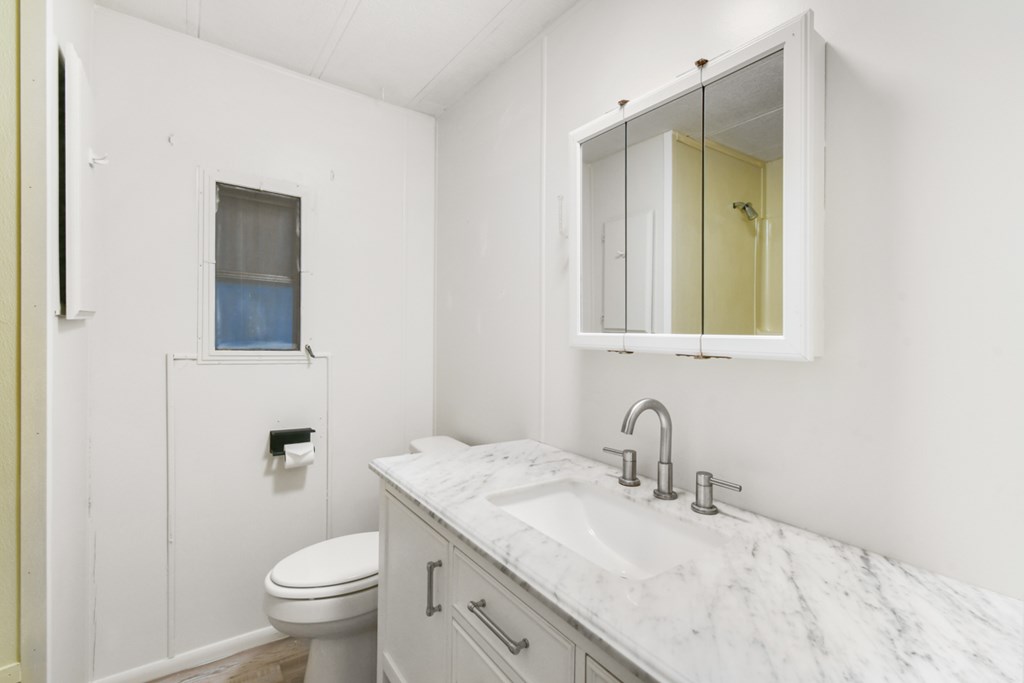 A white bathroom with a toilet, sink and mirror.