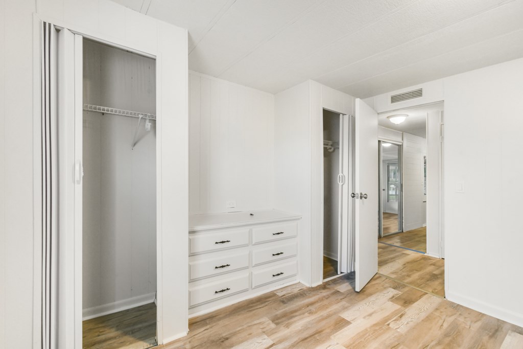 A white room with a wooden floor and a white wardrobe with a mirror.