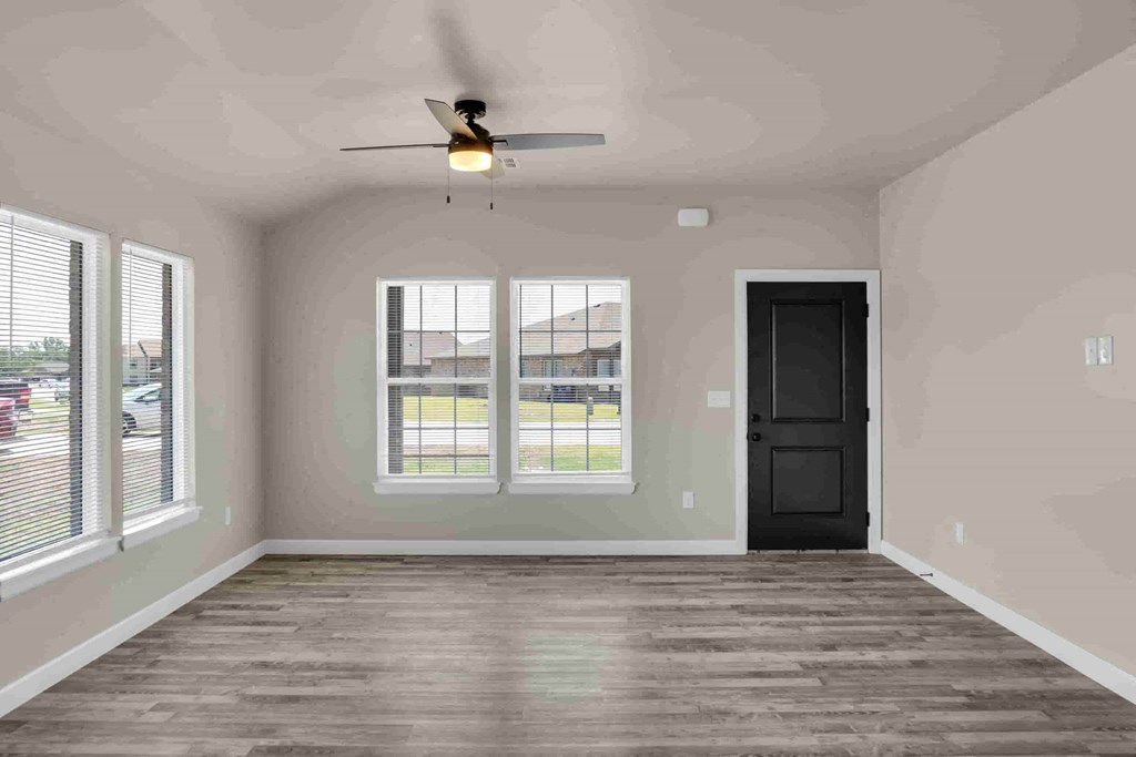 an empty living room with a ceiling fan and three windows