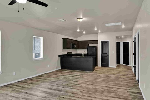 an empty living room with a kitchen and a ceiling fan