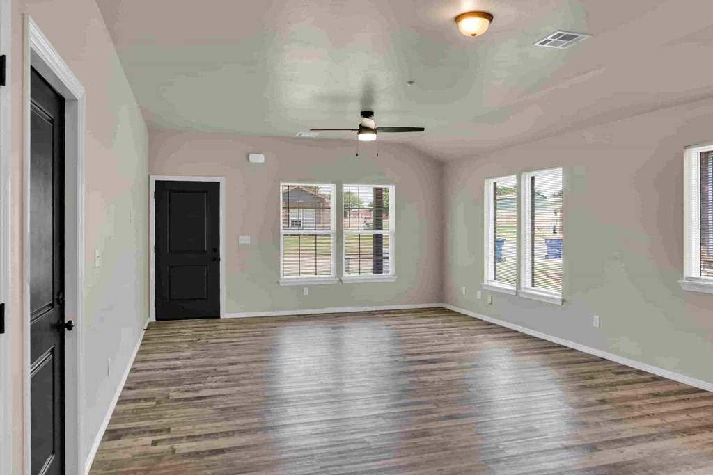 an empty living room with a black door and a ceiling fan