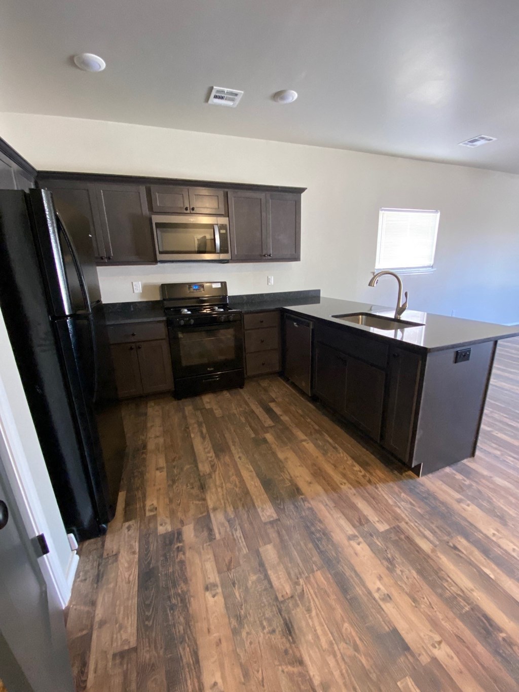 an empty kitchen with wooden floors and black appliances