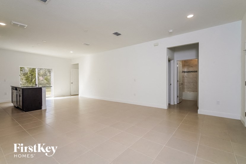 an empty living room with white walls and tile flooring and a door to a