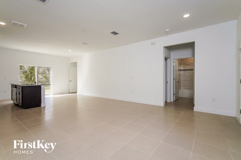 an empty living room with white walls and tile flooring and a door to a