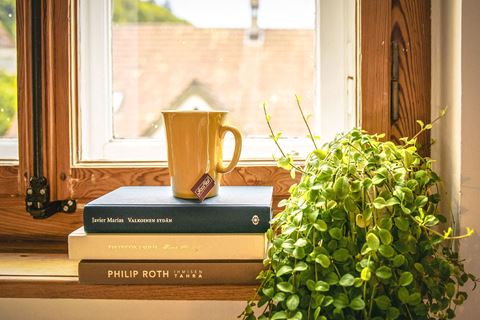 a stack of books sitting on a window sill next to a cup of coffee