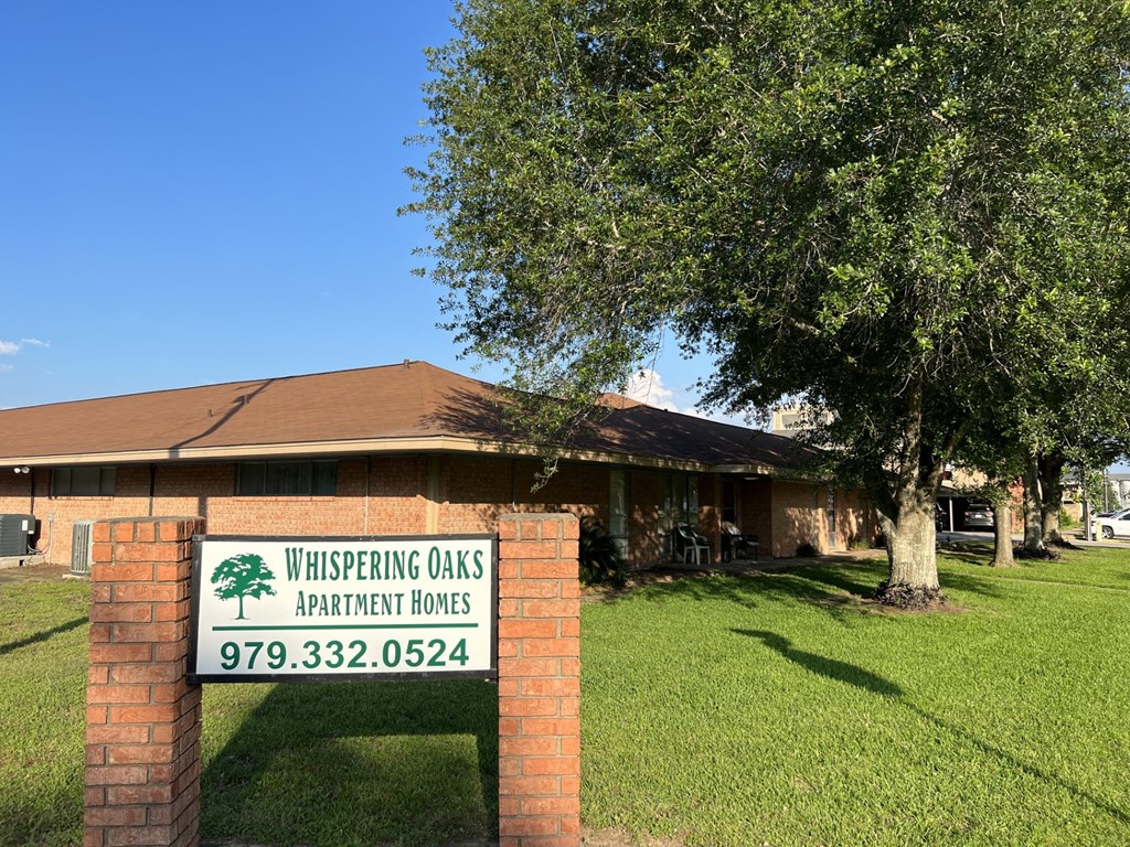 A sign for Whispering Oaks Apartment Homes stands in front of a building.