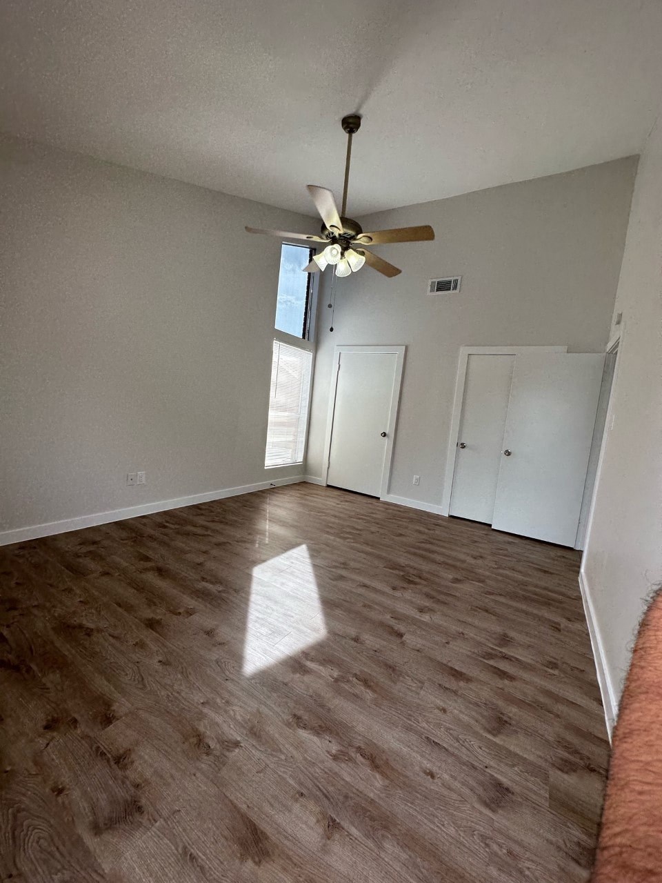 A room with a ceiling fan and light, hardwood floors, and white walls with two doors.