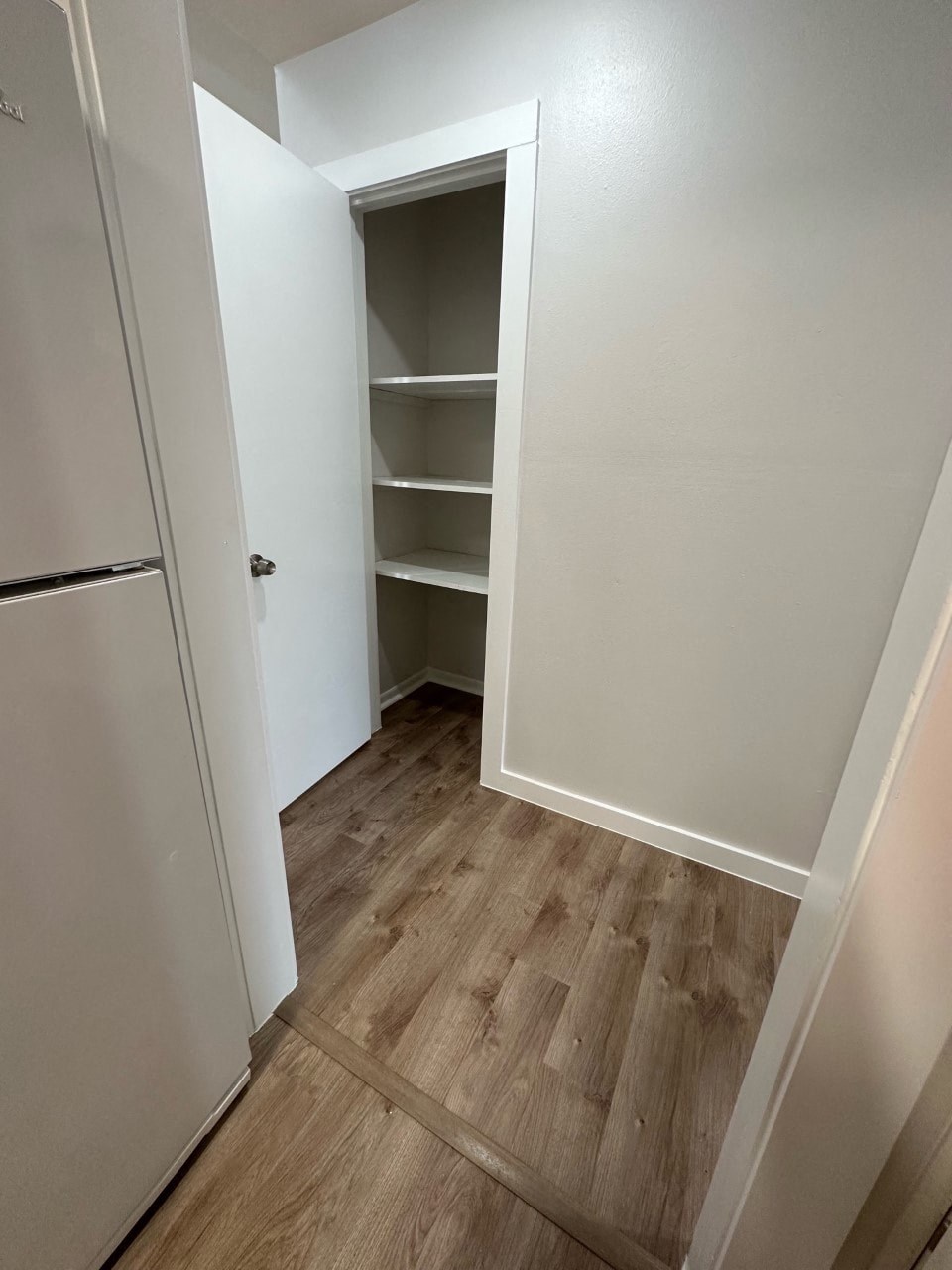 A white refrigerator is in a kitchen with wood flooring.