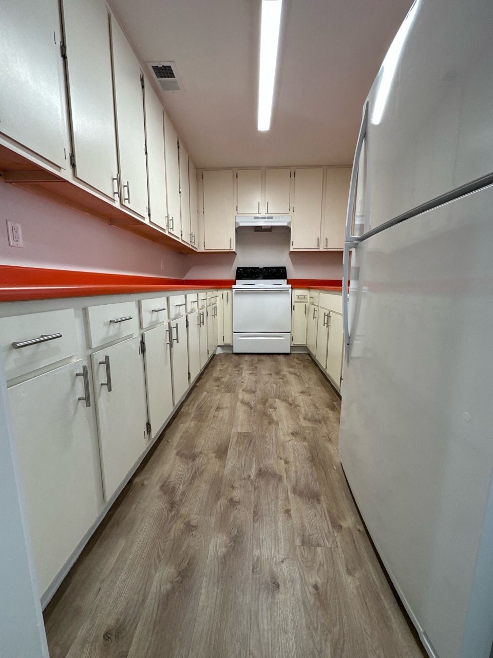 A long hallway of white cabinets with a white refrigerator on the end.
