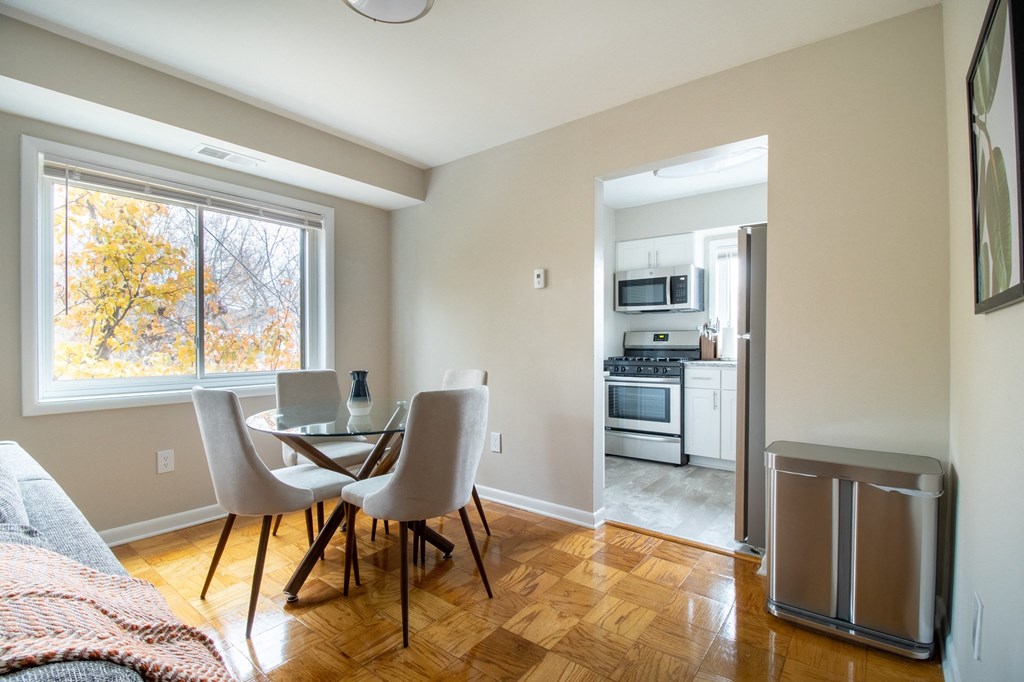 a living room with a dining room table and chairs and a kitchen with a refrigerator