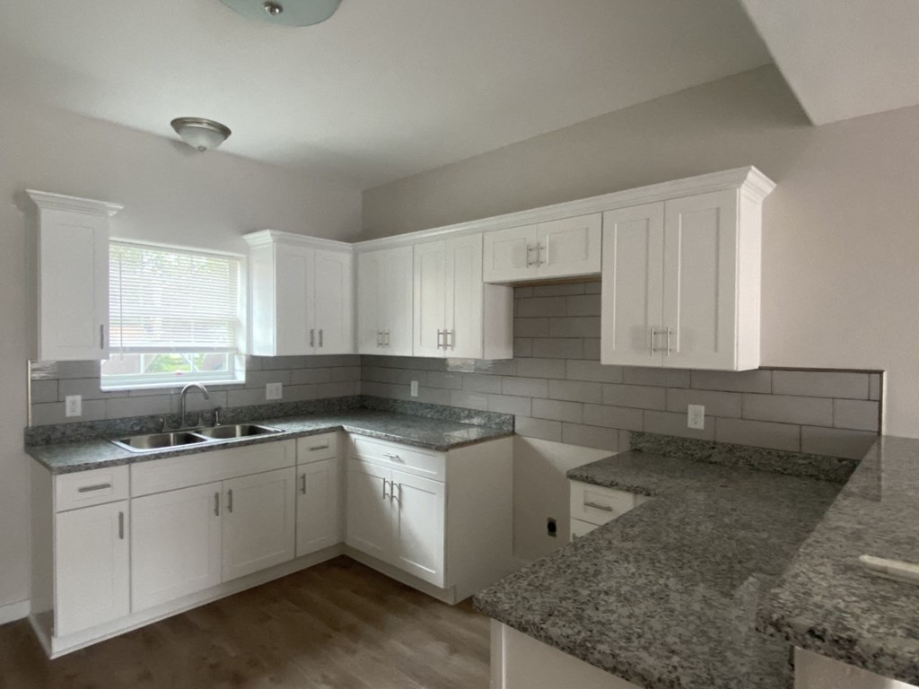 an empty kitchen with white cabinets and granite counter tops