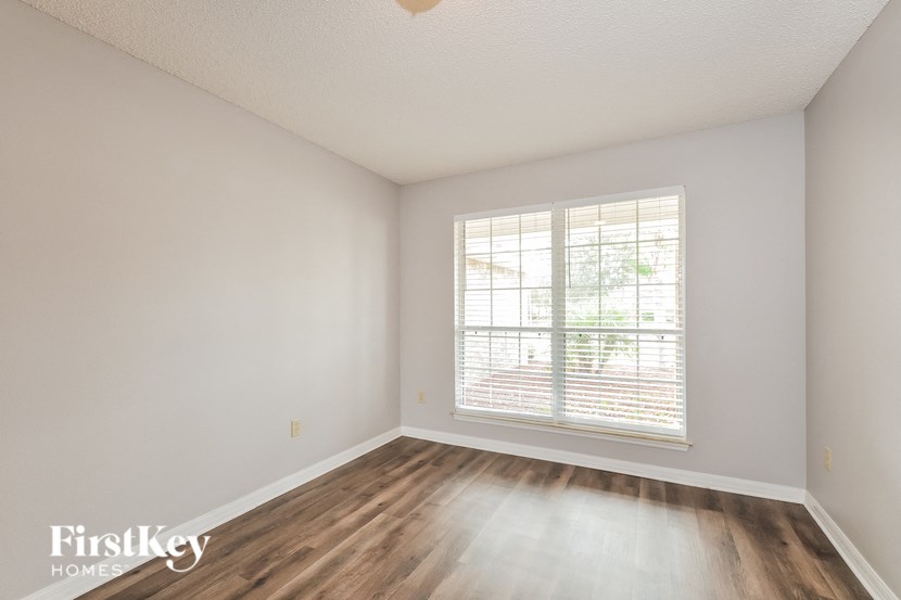 a bedroom with white walls and wood floors and a window