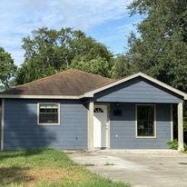 a small blue house with a driveway and trees