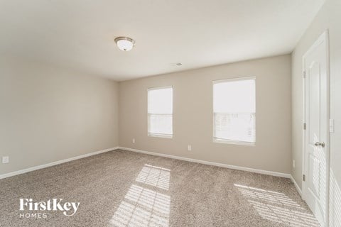 a spacious living room with carpet and two windows
