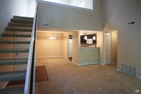 an empty living room with a staircase and a kitchen
