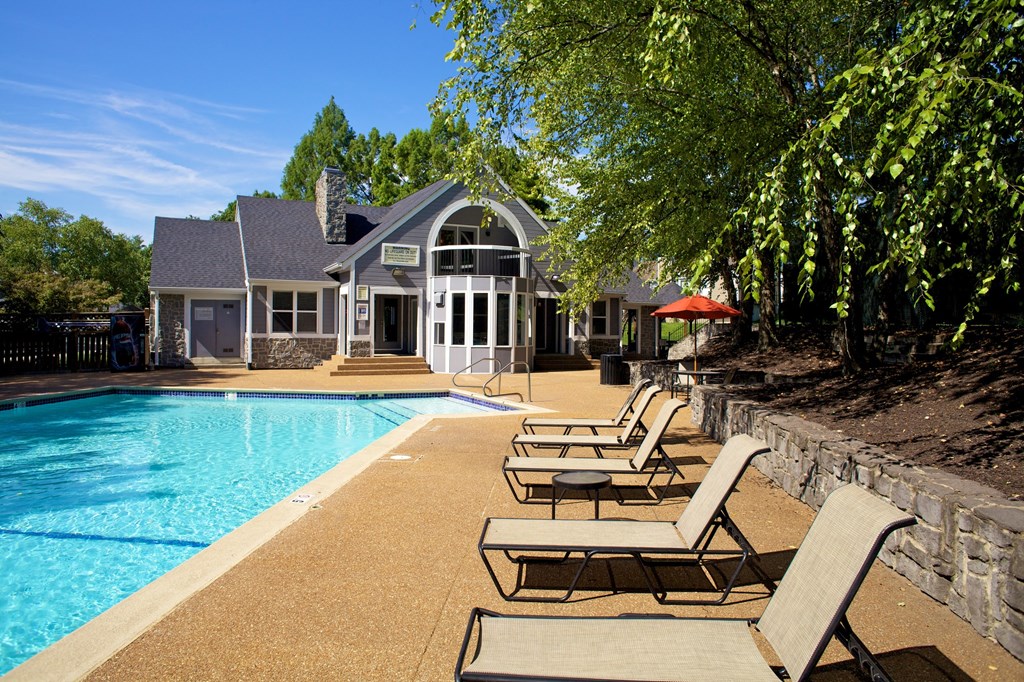 a swimming pool with chaise lounge chairs in front of a house