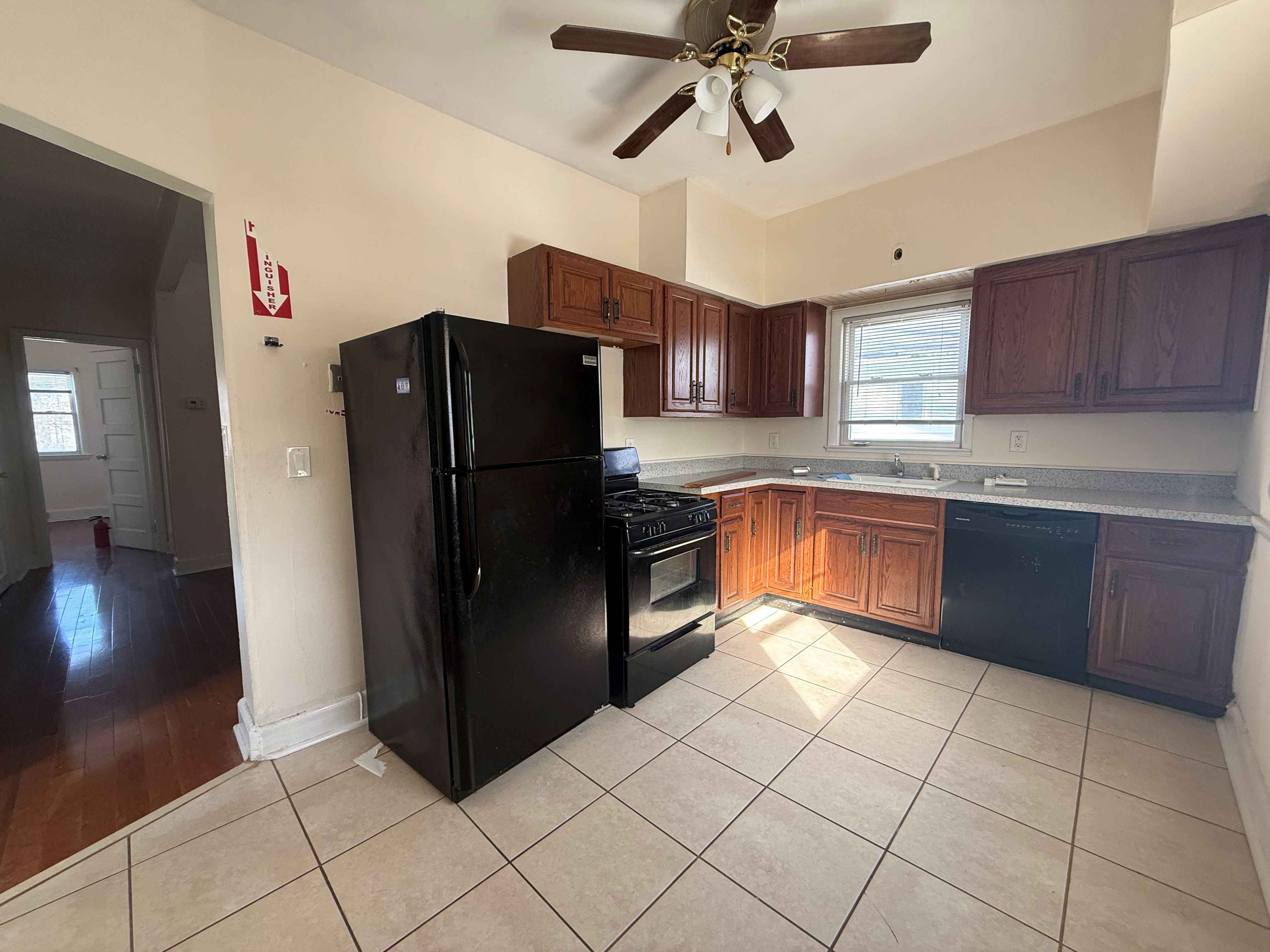 A black refrigerator in a kitchen with brown cabinets and a ceiling fan.