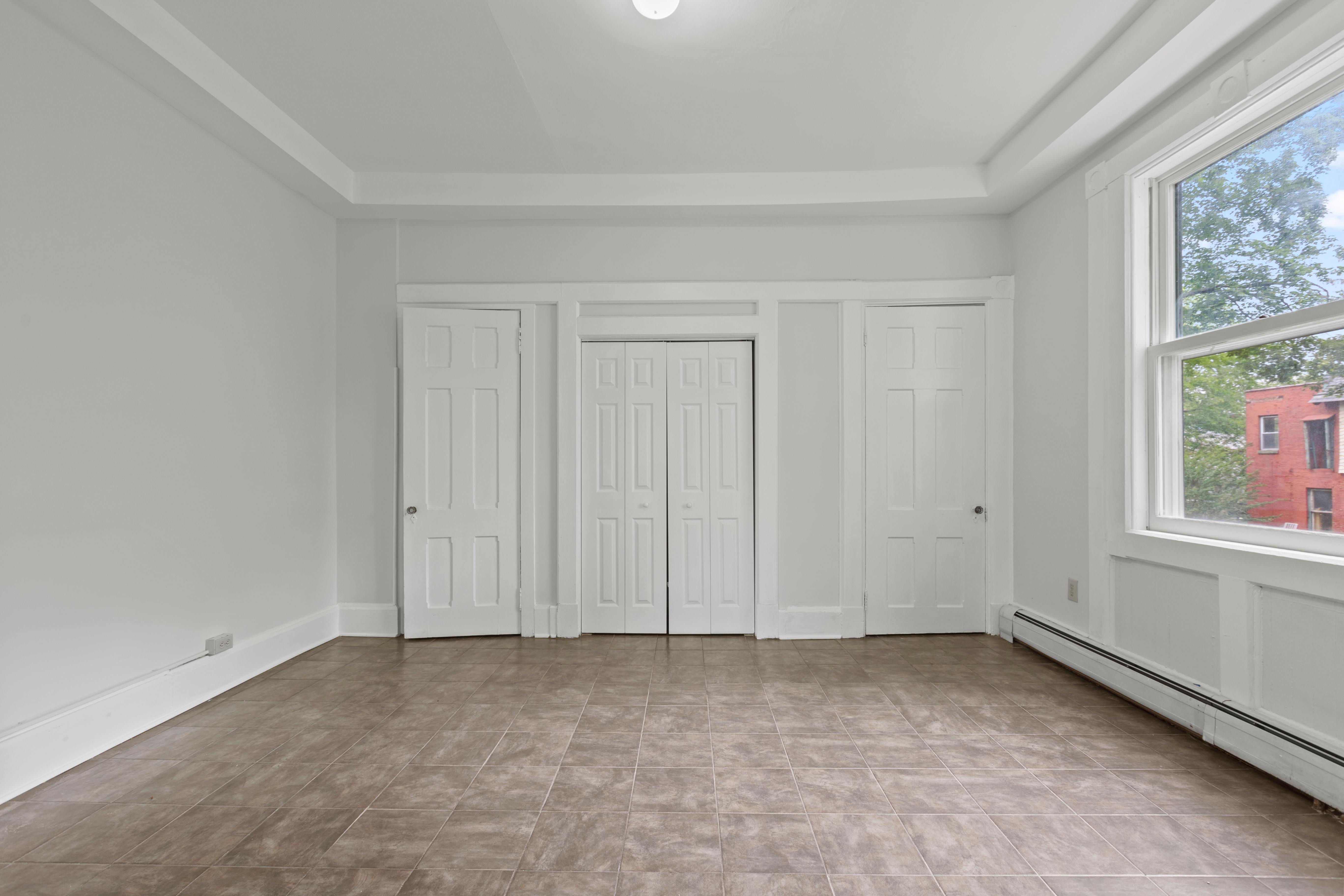 A room with white walls and a large window with a view of a red building outside.
