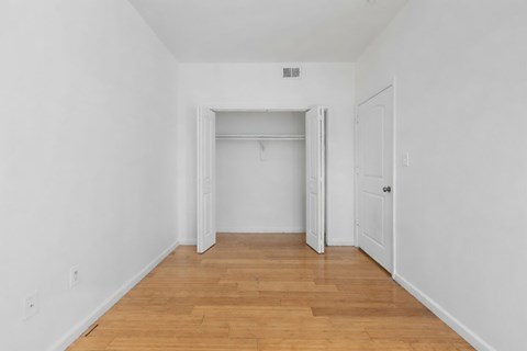 A room with white walls and wooden flooring with a doorway leading to another room.