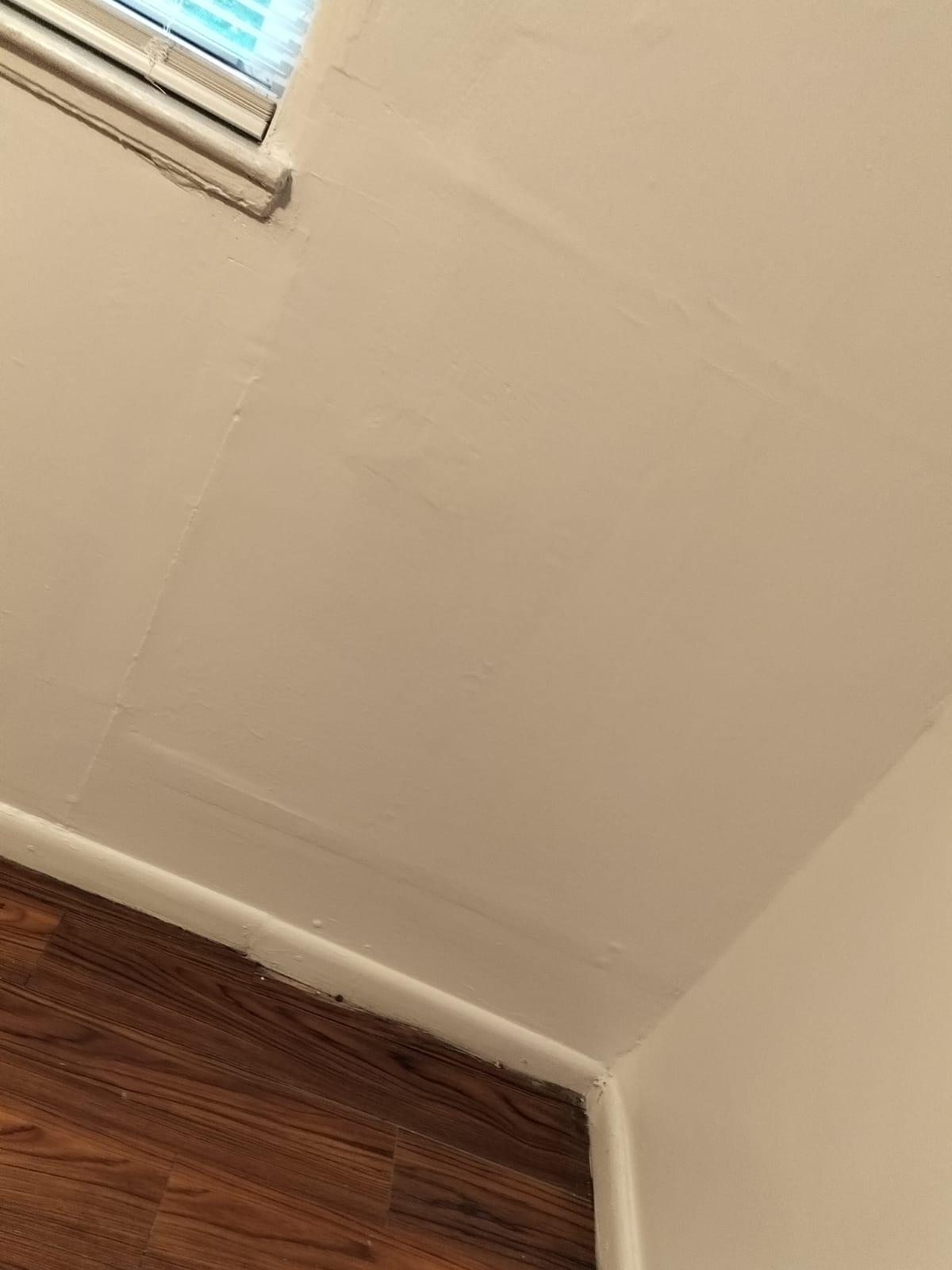 A corner of a room with a window and wooden flooring.