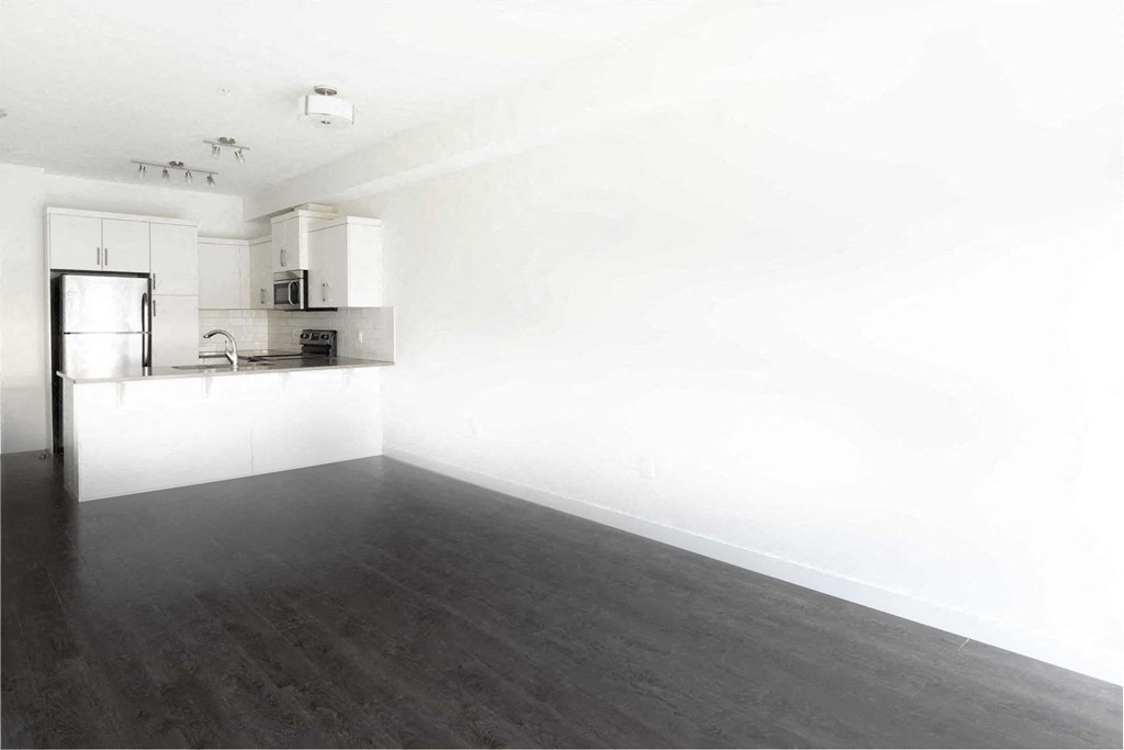 an empty living room with white walls and a kitchen