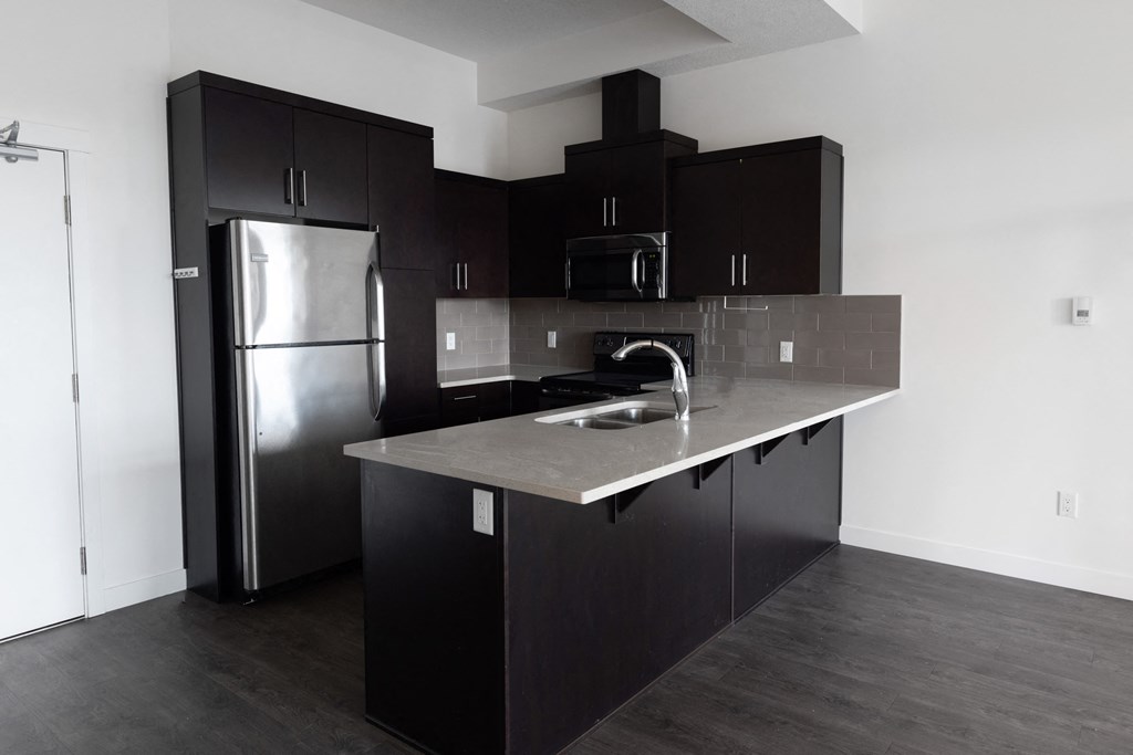 an empty kitchen with black cabinets and a stainless steel refrigerator