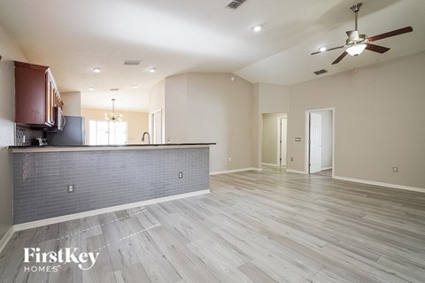 an empty living room with a kitchen and a ceiling fan